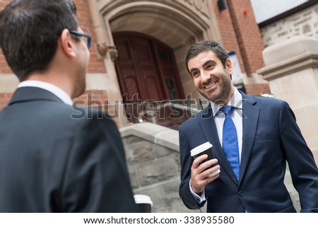 Two businessmen talking outdoors while taking coffee break