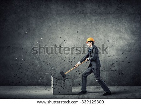 Young businessman in helmet breaking stone with hammer