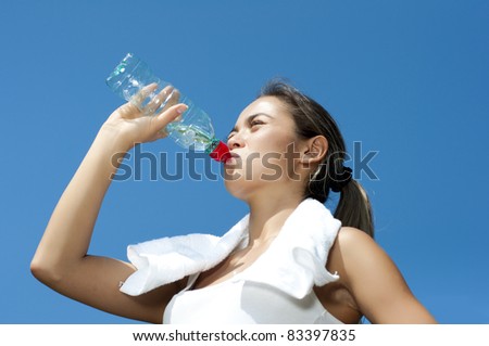 Young woman drinking water after exercise, summer park background
