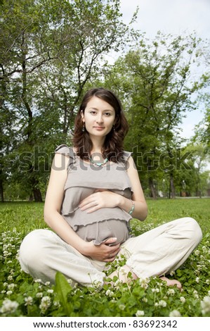 The portrait of the beautiful pregnant woman, sits on a grass
