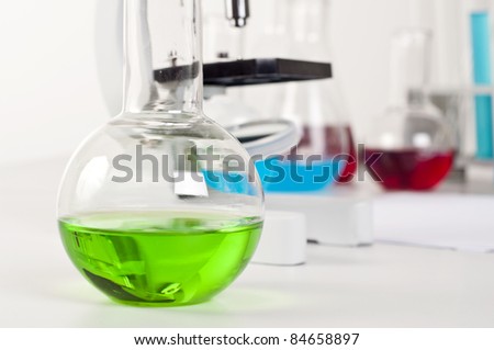 lab bottle with green liquid, in the background microscope and other items