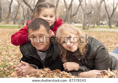 The young family in park, sits on a grass and smiles