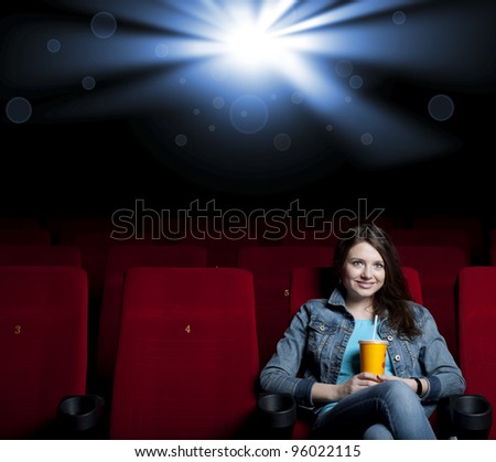 beautiful woman in a movie theater, watching a movie and drink a drink