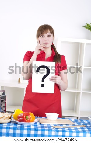 Young woman cooking fresh meal at home and holding question sign