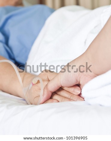 Elderly woman patient in bed with one hand being hold by daughter to be supportive