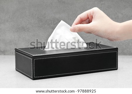 Close up of a woman's hand pulling a facial tissue from a black tissue box