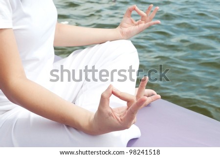 Hands of attractive young asian woman practicing yoga meditation at sunrise by the ocean