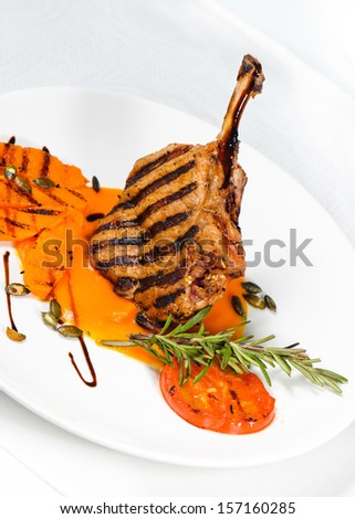 Veal on the bone. Grilled meat ribs on white plate with tomatoes and sauce in pumpkin