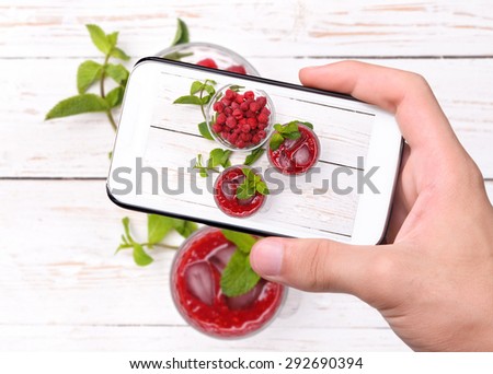 Hands taking photo raspberries drink with smartphone.