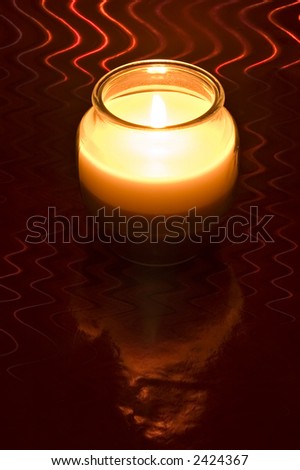 Red and white candle in glass jar with flame on red shiny background