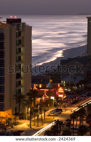 view of ocean at night between buildings with bright neon signs and streaks of lights