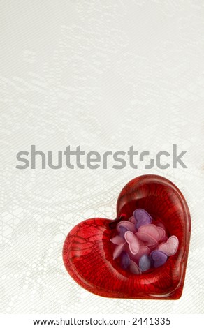 Red glass heart filled with pink, blue and purple hearts on white lace background