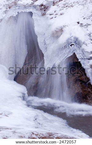 Ice and snow with waterfall flowing from under ice overhang