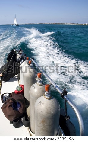 View of scuba tanks and boat wake with sailboat in the distance