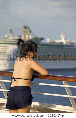 asian female tourist in bikini leaning on ship railing with cruise ship in background