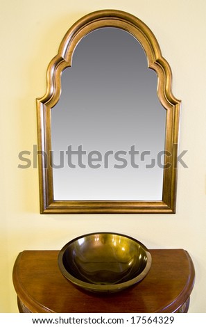large wall mounted reflective mirror with decorative wooden frame hanging above small table with bowl