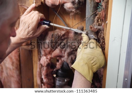a man tries to repair a broken pipe in his house wall