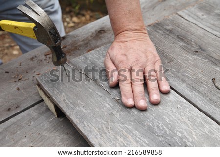 Man hammers old nail into weathered fence boards.
