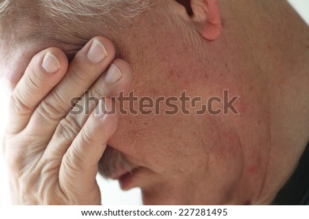 Depressed older man averts his head, covering his eyes with a hand.
