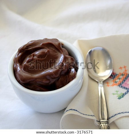 a bowl of chocolate pudding in a white bowl with a silver spoon and a unique, colorful napkin