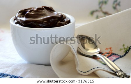 a small cup of chocolate pudding with a silver spoon on a vintage napkin and tablecloth