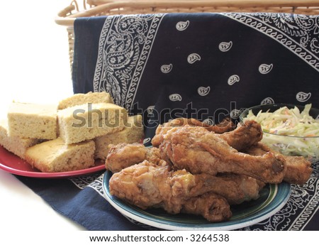 fried chicken legs, cornbread, and coleslaw on a dark blue bandanna draped over a wicker hamper for a July 4th picnic