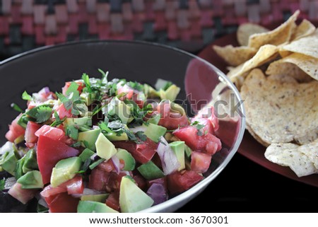 a bowl of chunky salsa with fresh tomatoes, red onion, avocados and cilantro with tortilla chips alongside