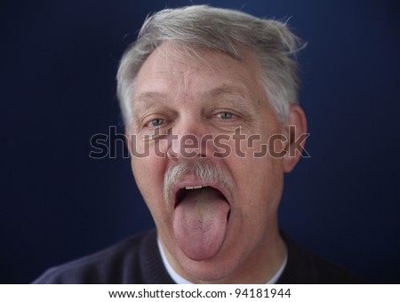 an older man sticks out his tongue as if for a medical exam