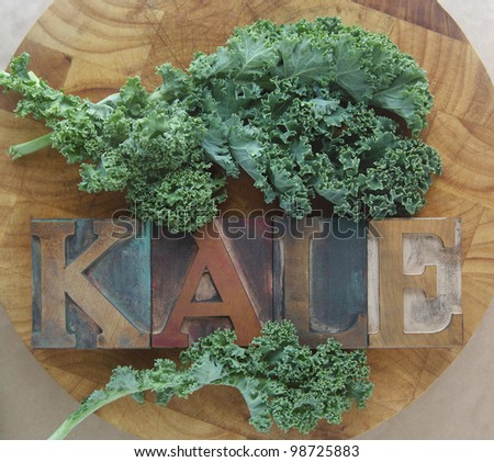 the word kale in old wood type with fresh leaves on a cutting board