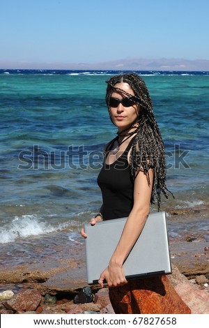 This young woman can be a professional freelancer or a student. She stands on a beach with her laptop.