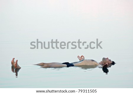 Man floating in a glassy water of dead sea with outstretched arms and chin mudra