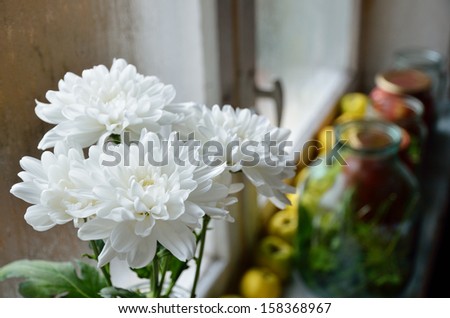 White chrysanthemums, quinces and sealed food jars are on the windowsill.
