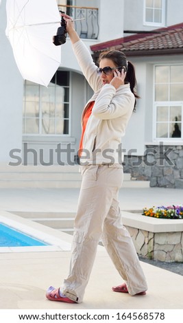 A model is posing against the wall outdoors. An assistant is holding a photo flash with an umbrella.