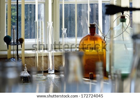 There are measuring cylinders, large bottles, glass flasks, metal support and bulbs  on the table in the chemical laboratory.
