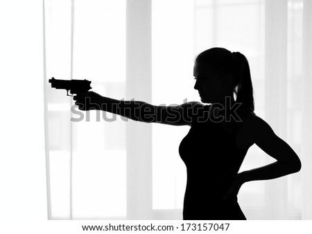 A slim young woman is aiming a pistol against the window.