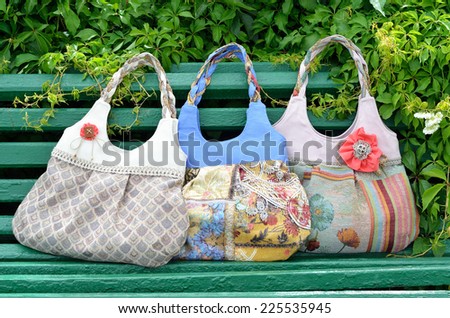 Three female handbags are on the bench. They are hand-crafted and made of the tapestry.