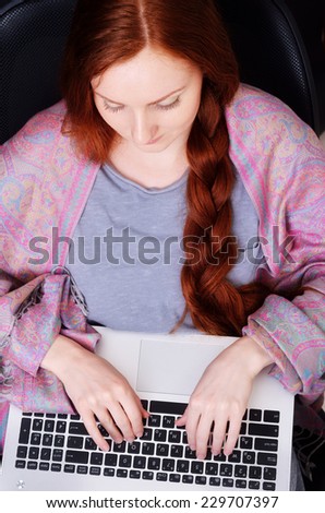 A young woman is sitting in the armchair at home. She types on a laptop.