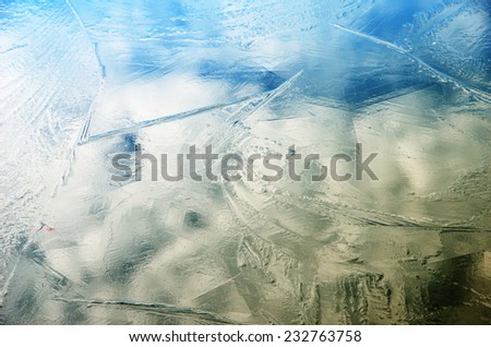 Thin ice crust covers the calm water. The sky with clouds are reflected in the water surface.