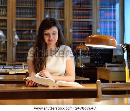 A young woman is reading a large book in the reading-room of a scientific library.