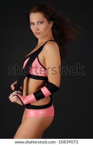 Girl in pink short and top with dark belts stands sideways , hair waved, black background