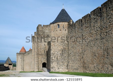Inner old defense wall with rough masonry and towers of Carcasson castle in sunlight against blue sky, France