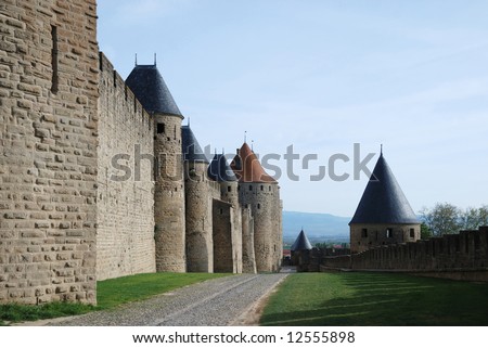Inner old defense wall with conic towers of Carcasson castle in sunlight against blue sky and road along, France