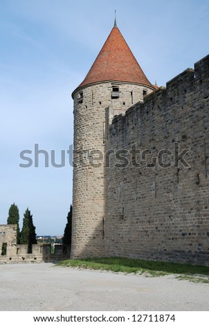 Old defense stone wall with loopholes and conic tower of Carcasson castle in sunlight against blue sky, France