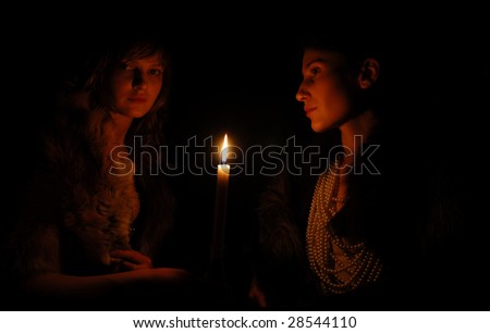 Serious girls around burning candle in the dark, side view