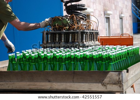 Green wine bottles are stowed with auto-loader on sunlit auto-truck. Accumulator car is in winery yard.