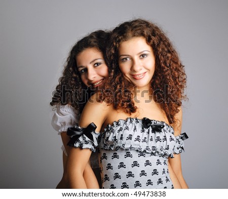 Young woman hugs her sister. The attractive girls are very much alike because they are gemini. They are looking at camera and smiling. Pretty twins are wearing fetching attires.