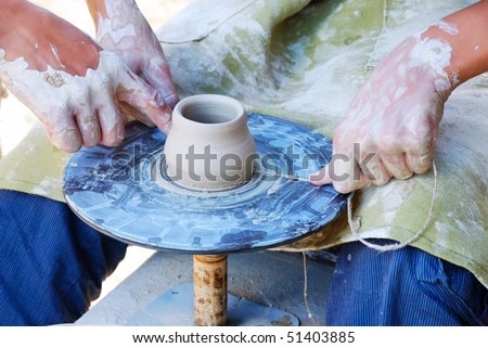 An apprentice is making pottery by the throwing wheel. He is helped by a master. In the photo we can see two pair of hands stained with clay and the jigger with a pot.