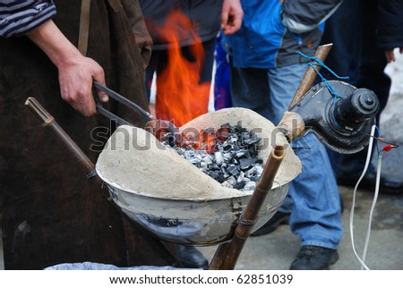 A farrier is working with portable forging furnace. In the photo we can see the human hand holding tongs with handicraft.