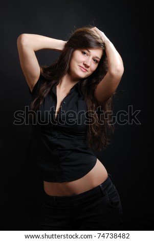 Teenage girl is photographed in low key against the dark background. Young woman is posing with pleasure. Her pretty belly are not covered with black blouse.