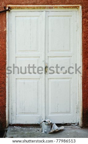 Old wood door is peeling away. There are tin of paint and brush in front of it. It is in need of repair.